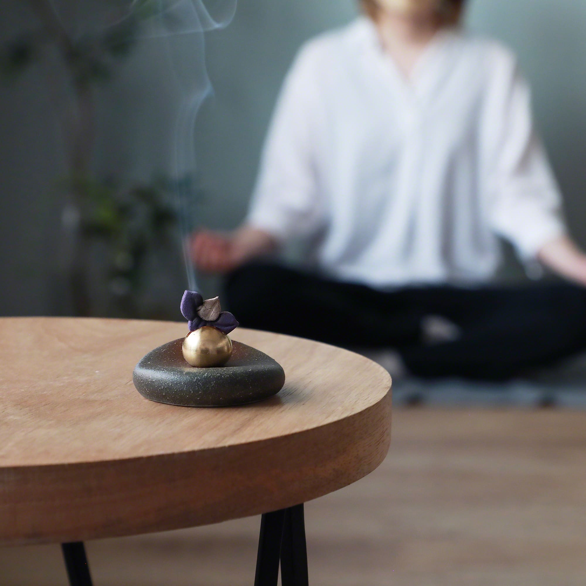 Lifestyle image of burning pressed incense on a table with a person meditating in the background