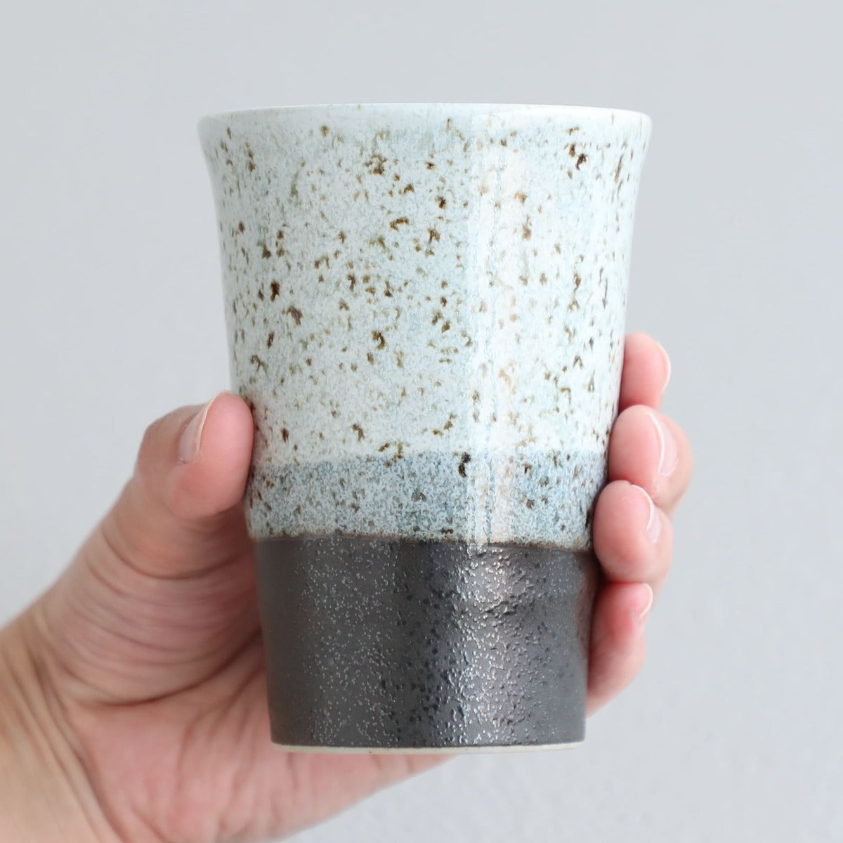 hand holding a grey ceramic cup