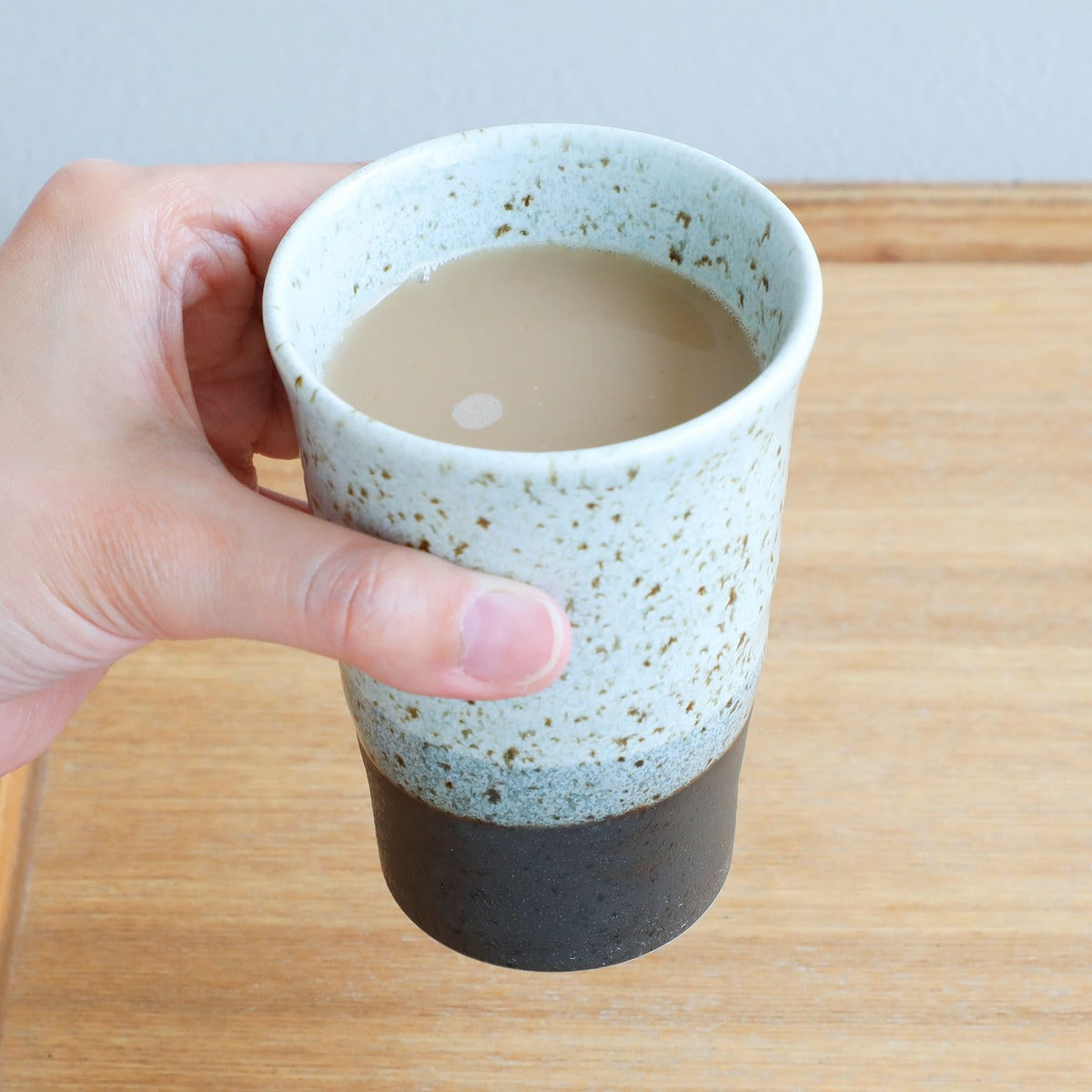 hand holdiong grey ceramic tea cup with tea inside