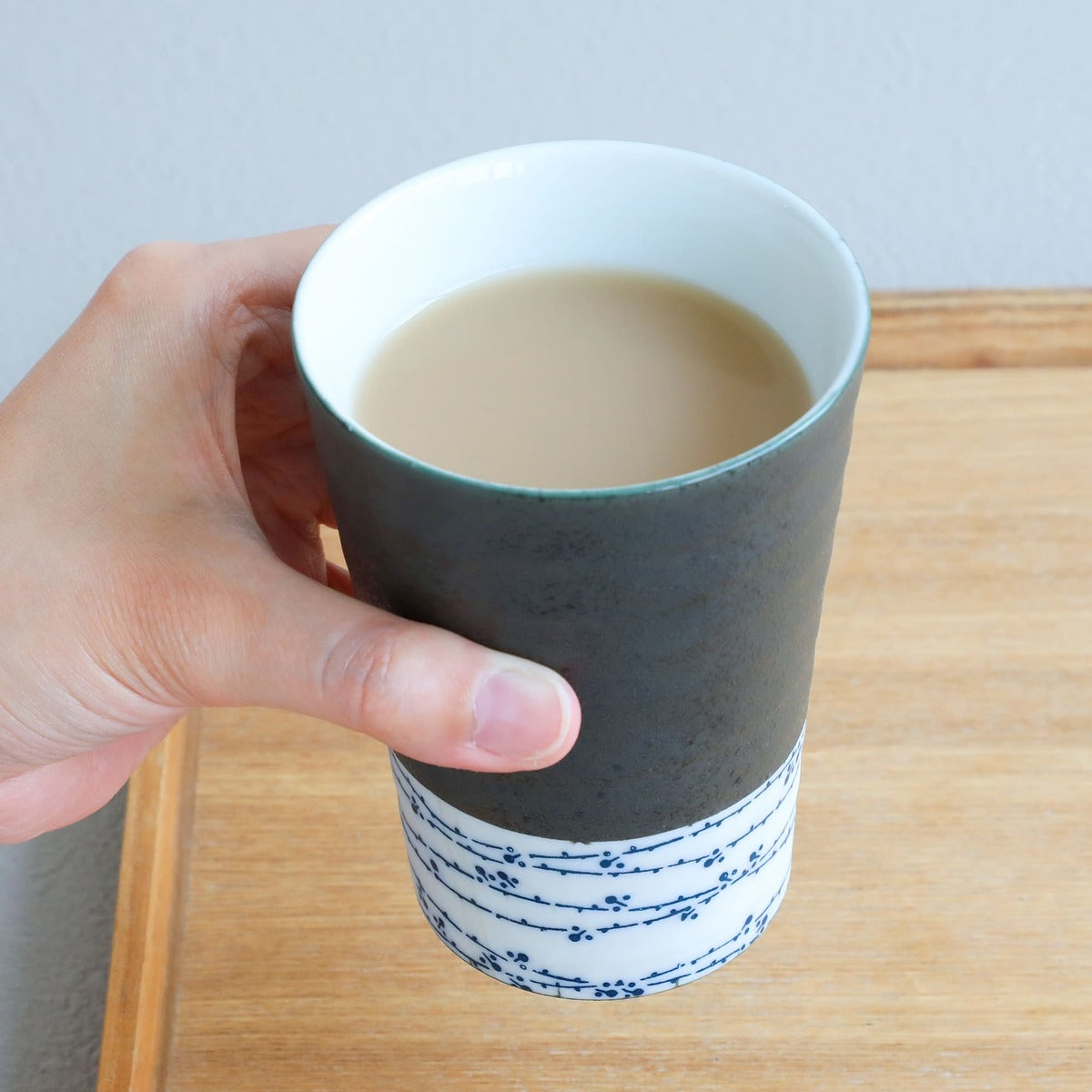 hand holding a grey and white tea cup with tea inside