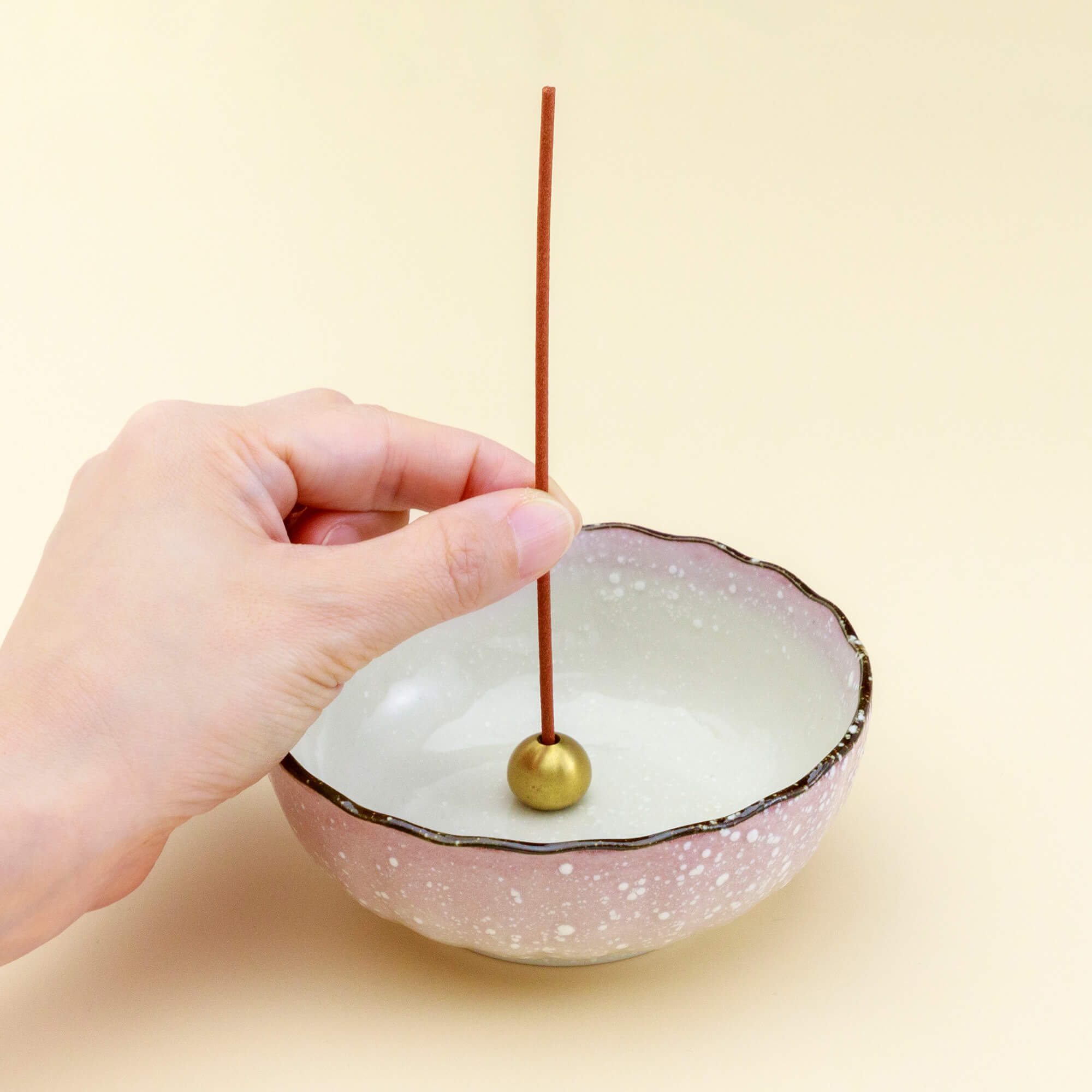 hand placing an incense stick in the ceramic incense holder