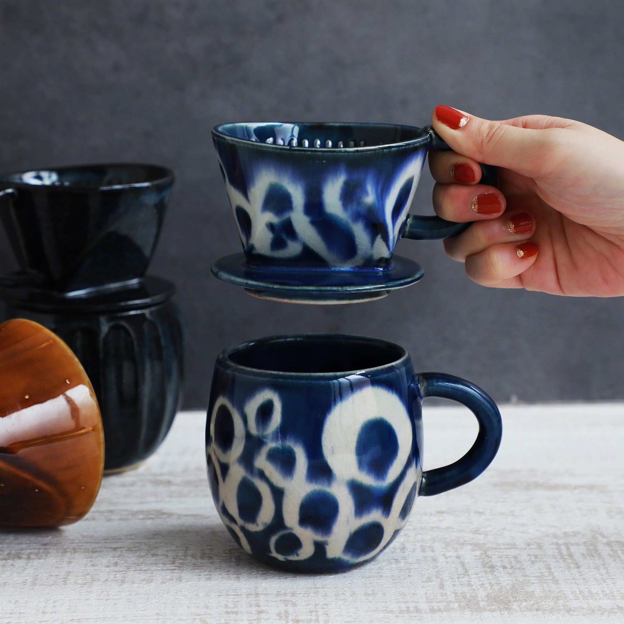 A hand holding the Asayu Japan Ceramic Coffee Dripper Ocean model over the matching accessory mug.