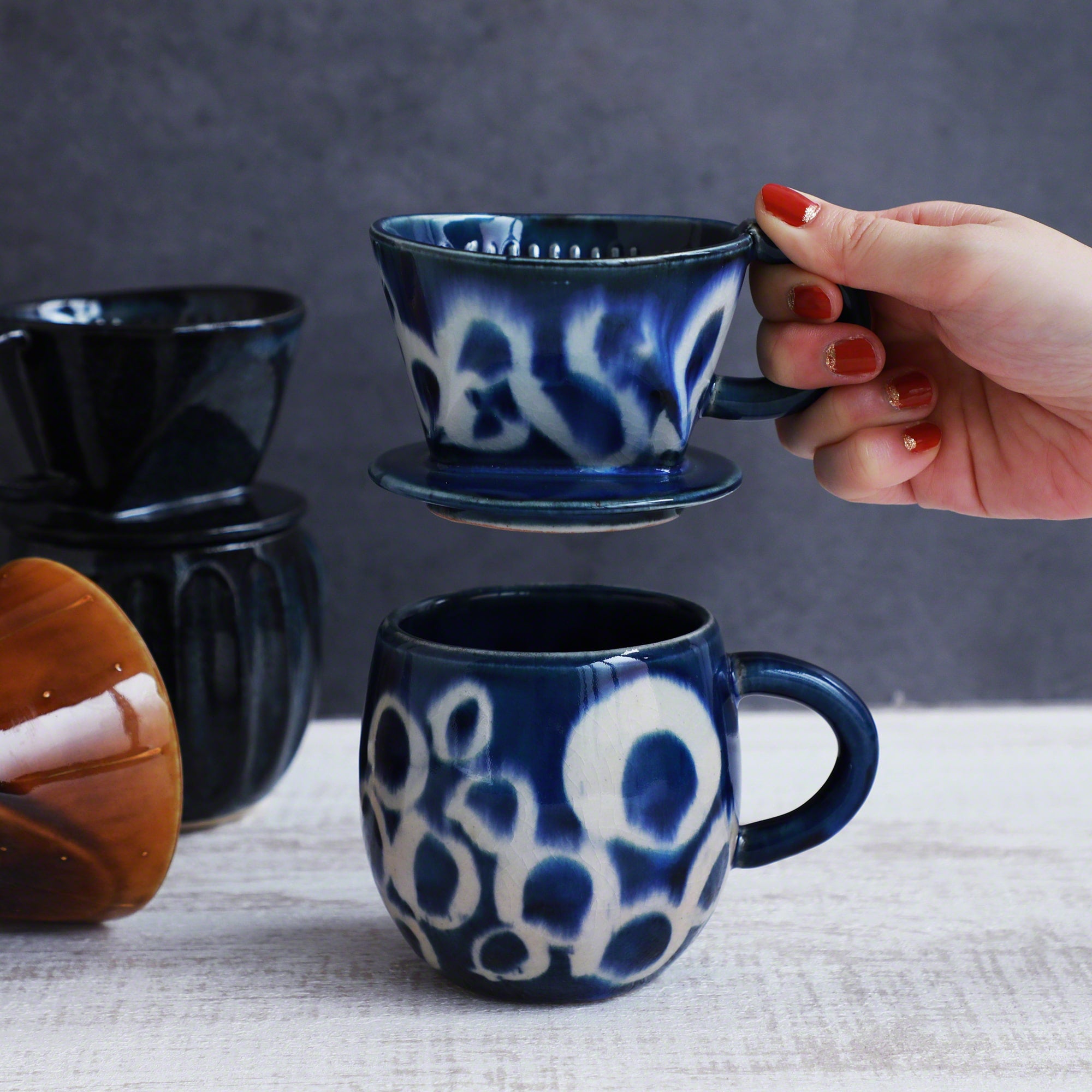 A hand holding the Asayu Japan Ceramic Coffee Dripper in Ocean blue over the matching accessory mug.