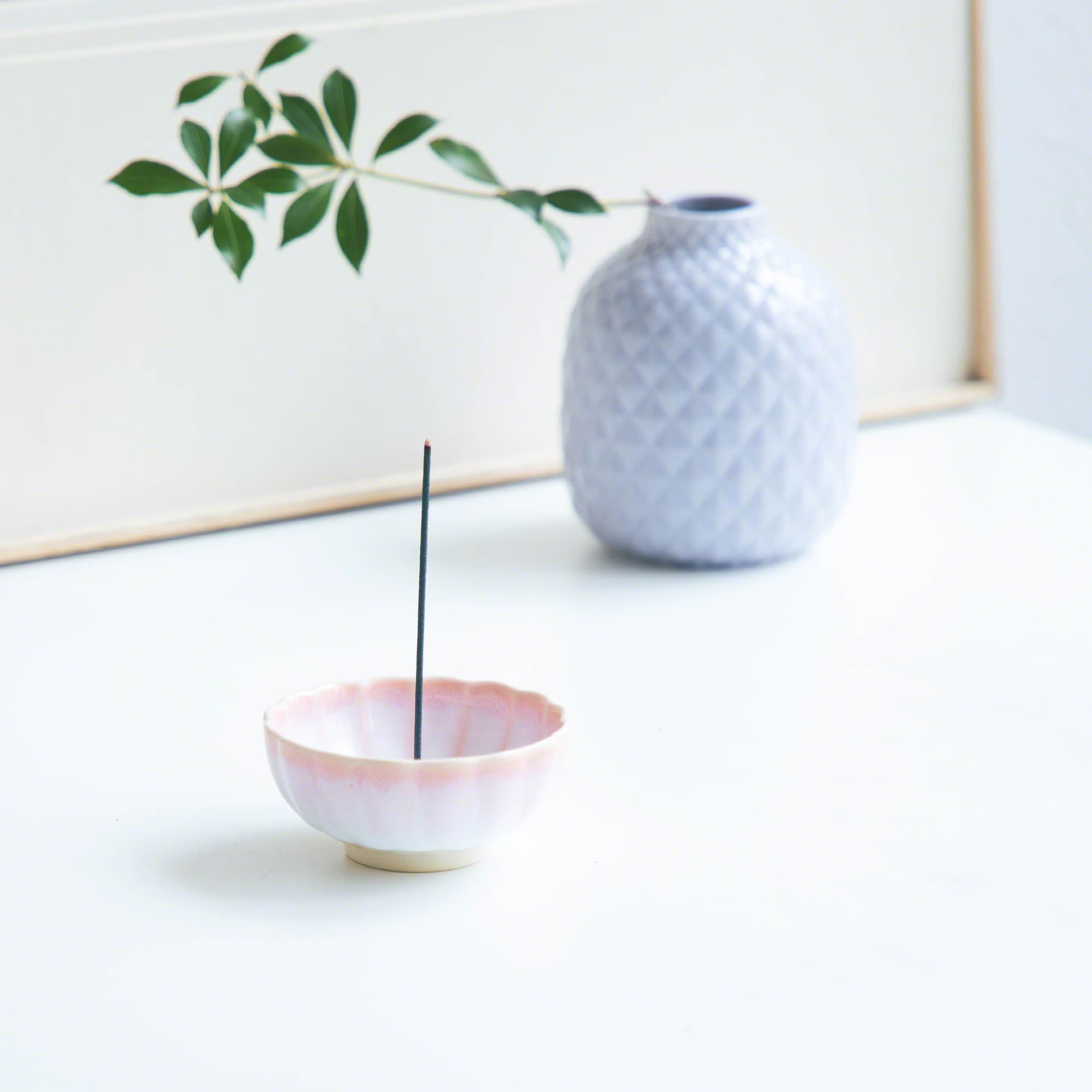 Cherry Blossom Pink Mini Lotus Incense Holder by Asayu Japan with a stick in a desk next to a vase with flowers.