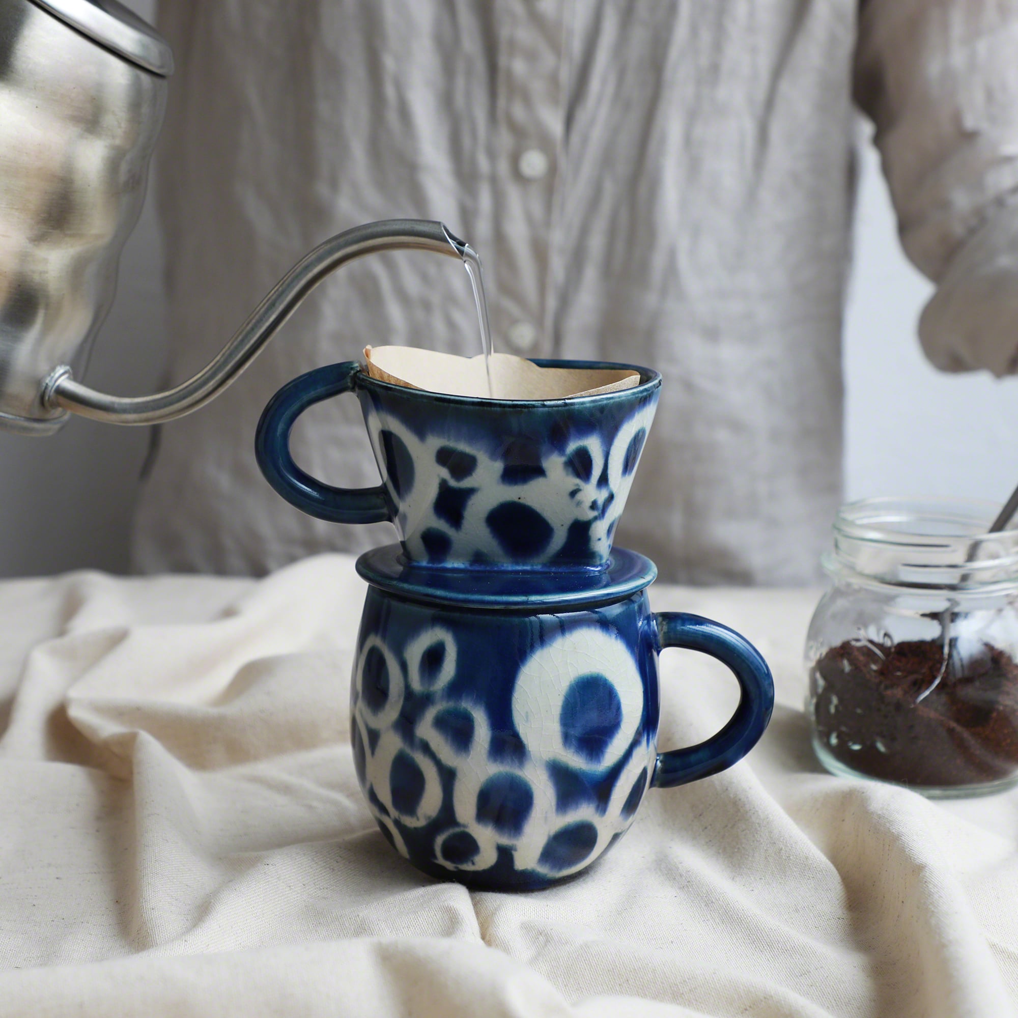 Pouring water over the paper filter on the mounted Asayu Japan Ceramic Coffee Dripper and Accessory Mug in ocean blue with white abstract pattern to make coffee