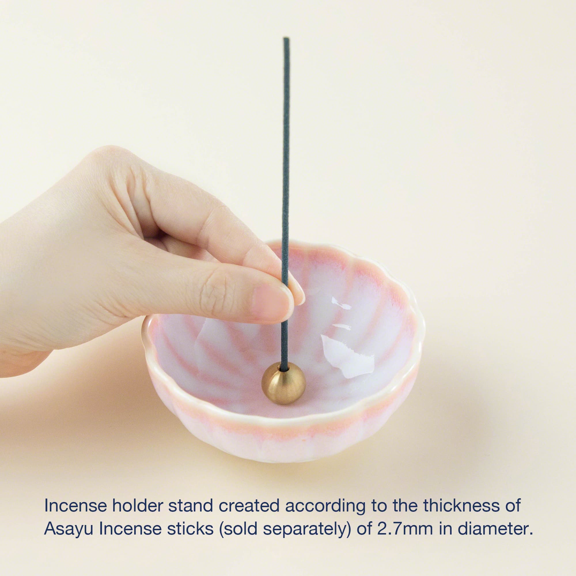 Cherry blossom pink ceramic incense holder with brass stand by Asayu Japan with a stick on it.