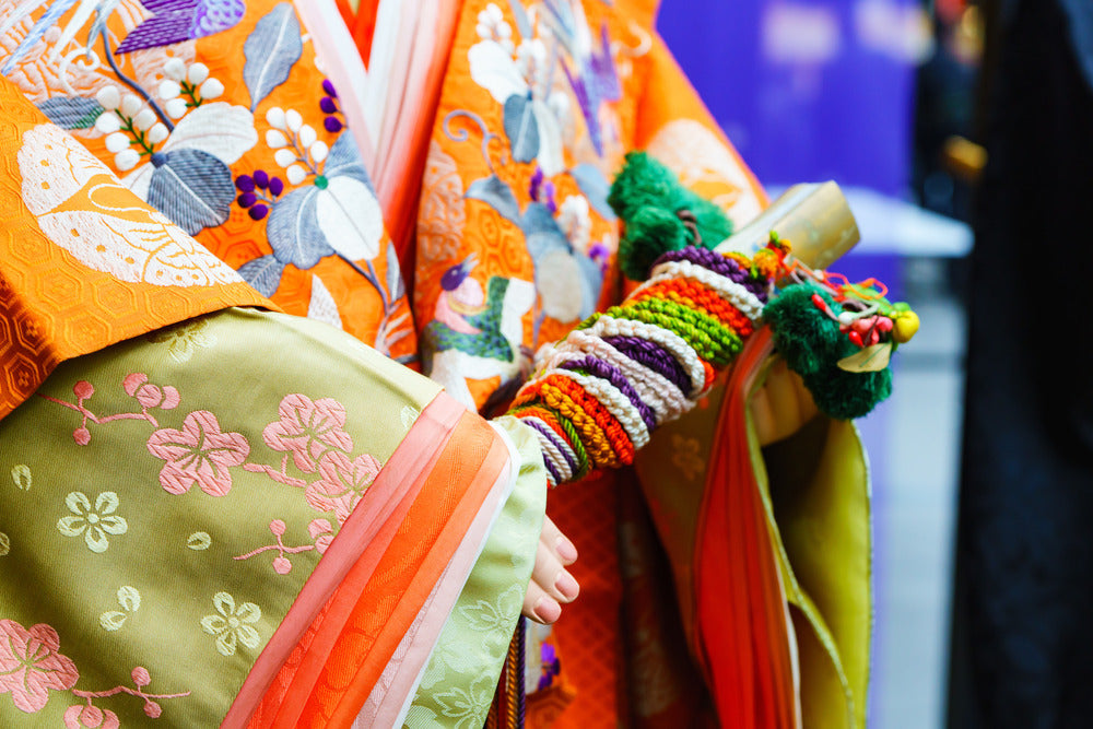 Zoom on details of a japanese traditional doll wearing a noble costum. The costume is vibrant and colourfull with clear contrast of shapes, design,, fabrics and layers.