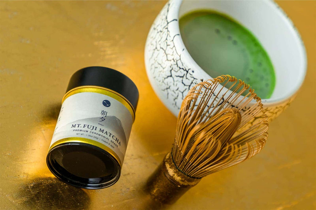 Matcha green tea canister, whisk, and bowl on a gold surface