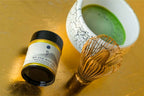 Matcha green tea canister, whisk, and bowl on a gold surface