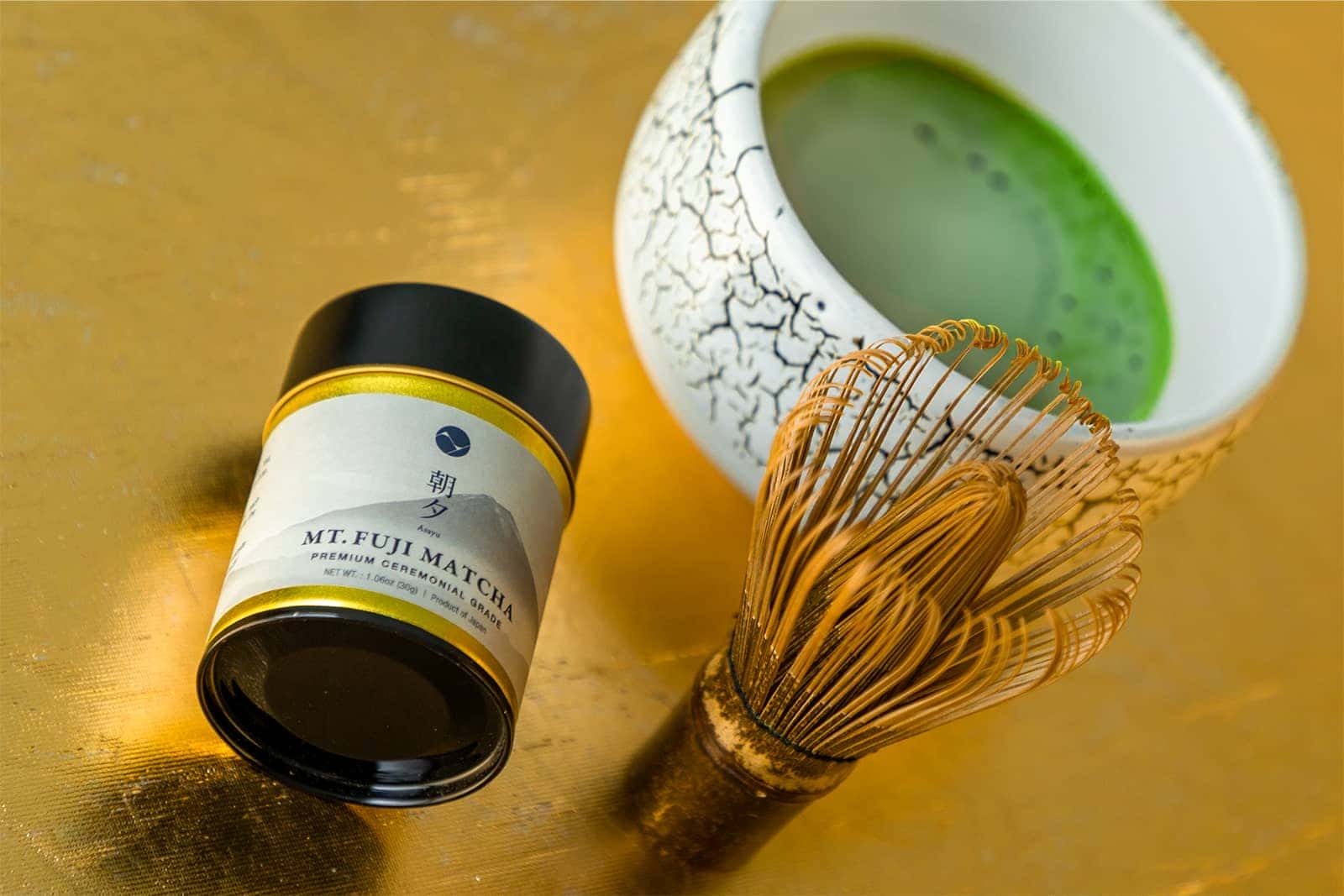 Matcha green tea canister, whisk, and bowl on a gold surface