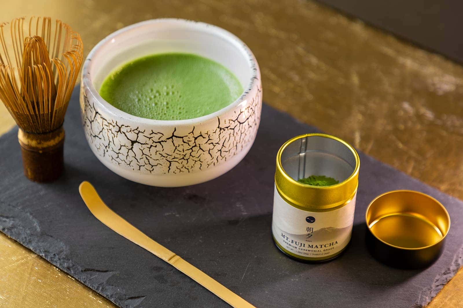 Matcha green tea set with a bowl, whisk, and container on a slate surface.