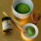 Matcha green tea set with a bowl of matcha, container of matcha powder, and whisk on a gold surface.