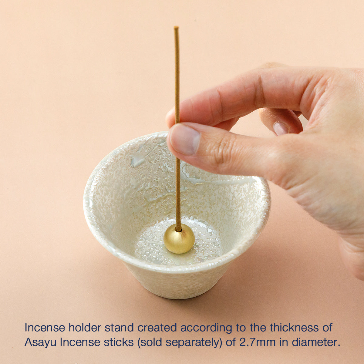 hand placing incense stick in cone shaped white incense holder 