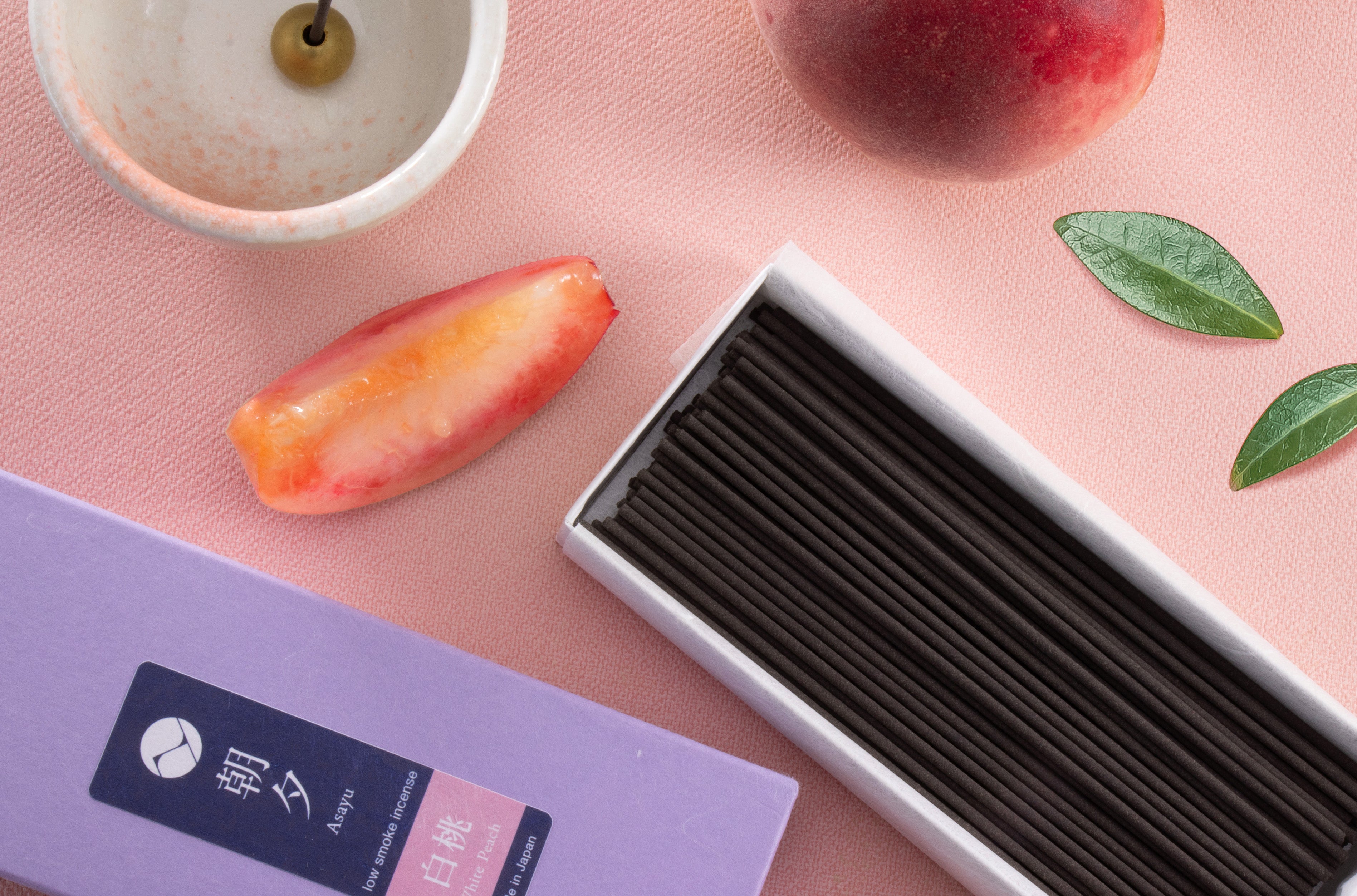 Peach incense sticks box 40g next to an incense holder and sliced peach
