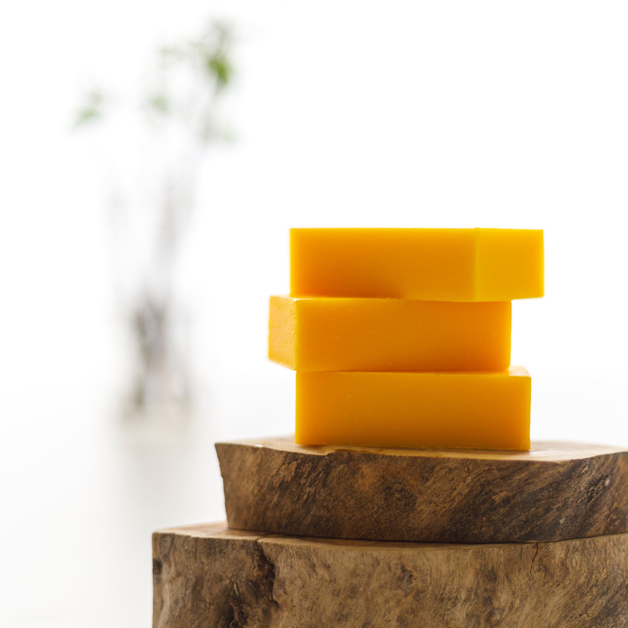 Stack of yellow soap bars on a wooden block with a blurred natural background