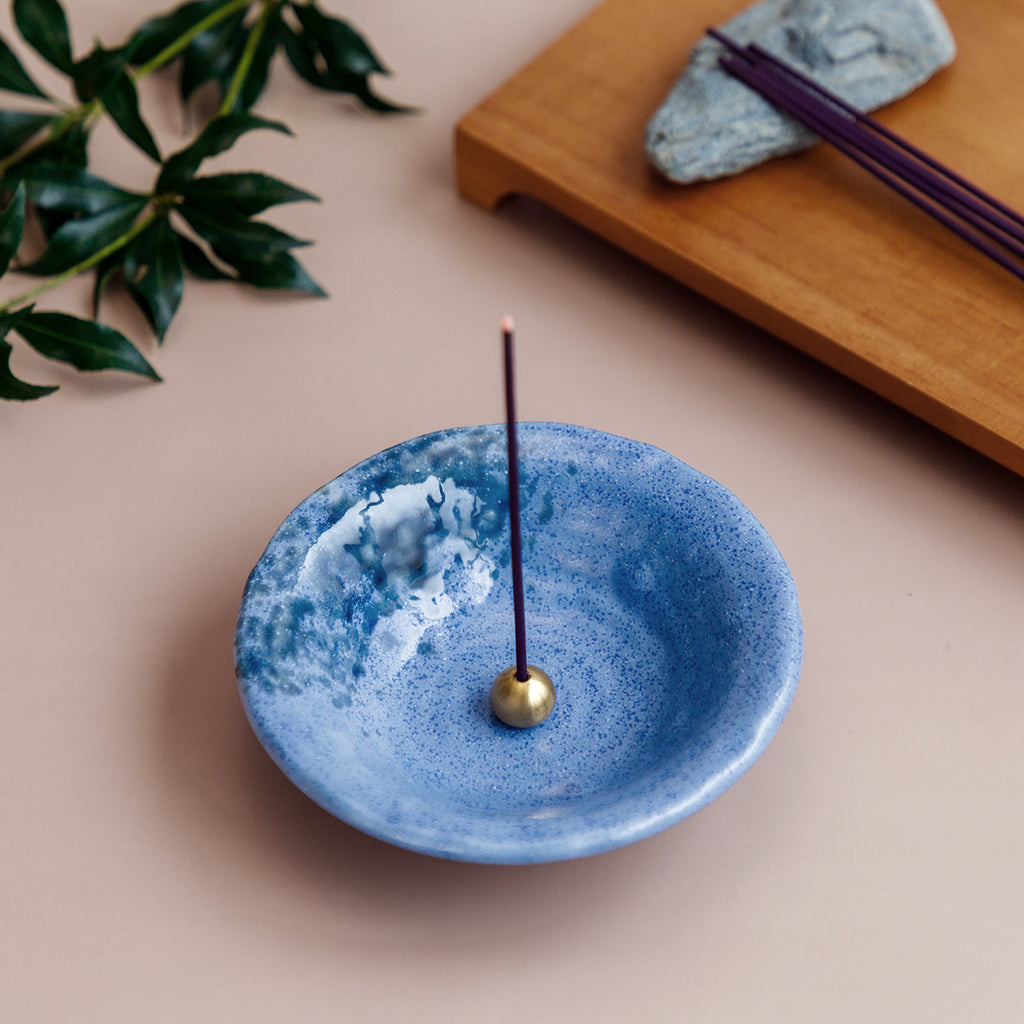 Incense burning in brass holder within a blue ceramic incense holder