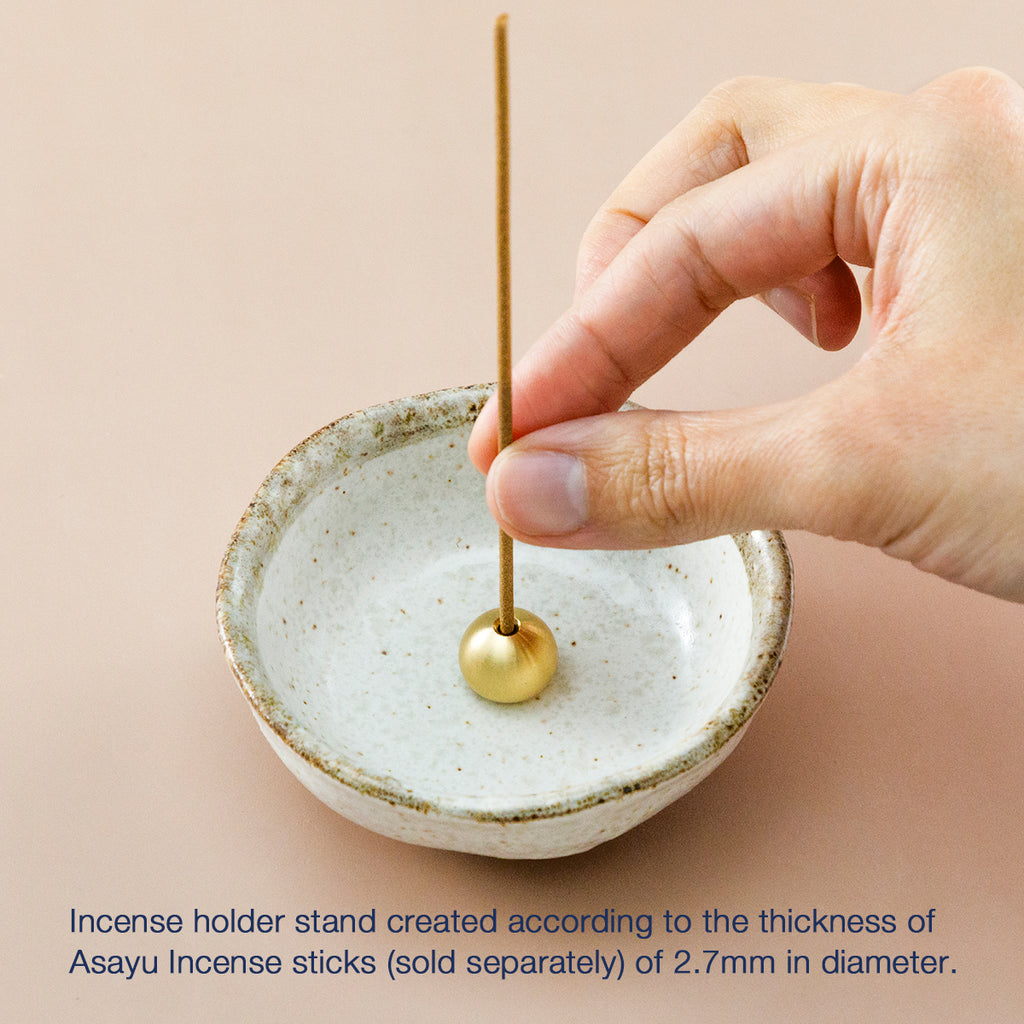 hand placing an incense stick in the white small incense holder