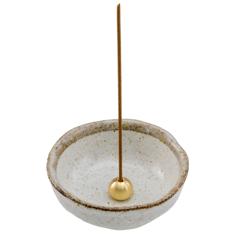 incense stick in brass holder within white ceramic holder