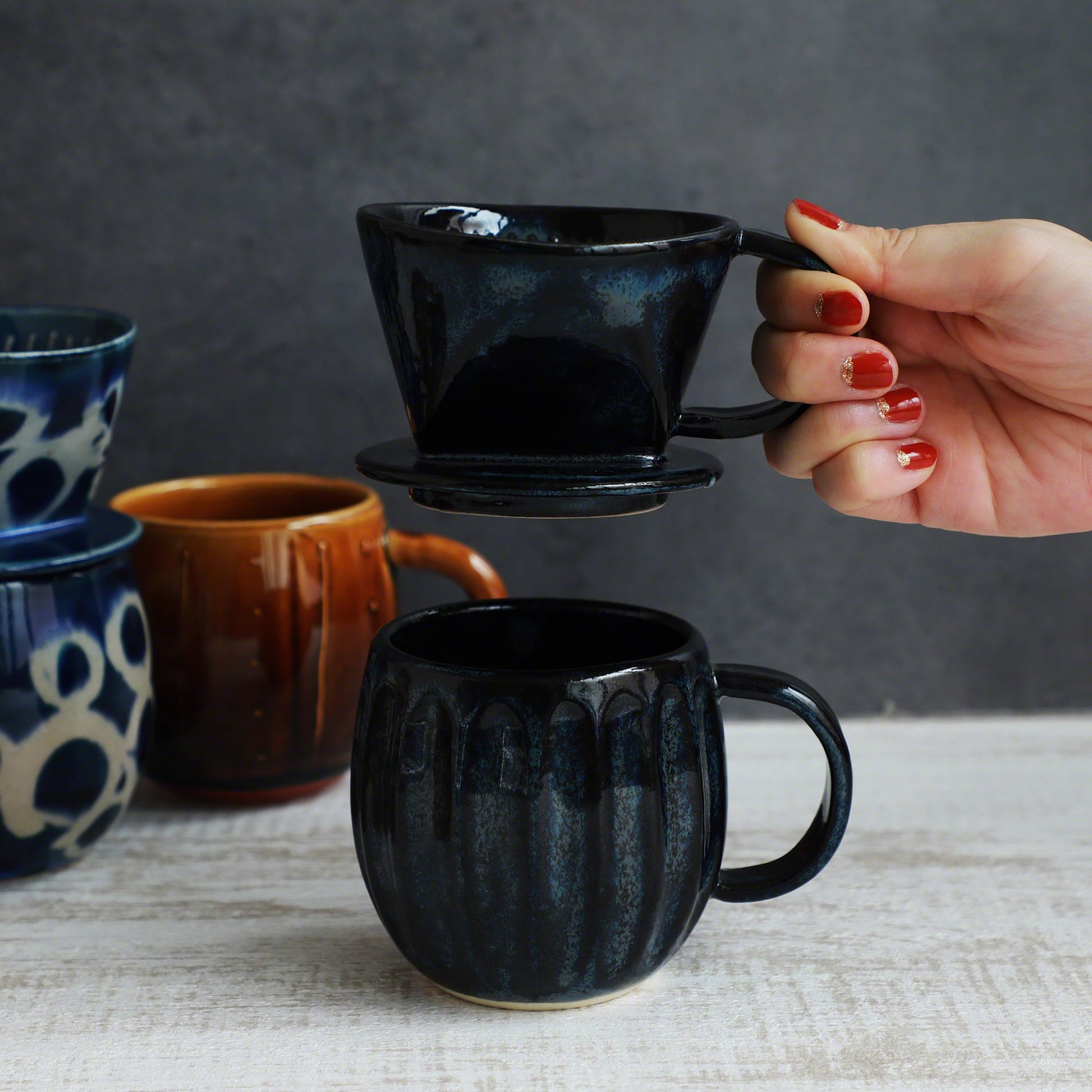 A hand holding the Asayu Japan Ceramic Coffee Dripper in dark navy blue over the matching accessory navy blue mug.