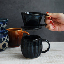 Lade das Bild in den Galerie-Viewer, A hand holding the Asayu Japan Ceramic Coffee Dripper in dark navy blue over the matching accessory navy blue mug.
