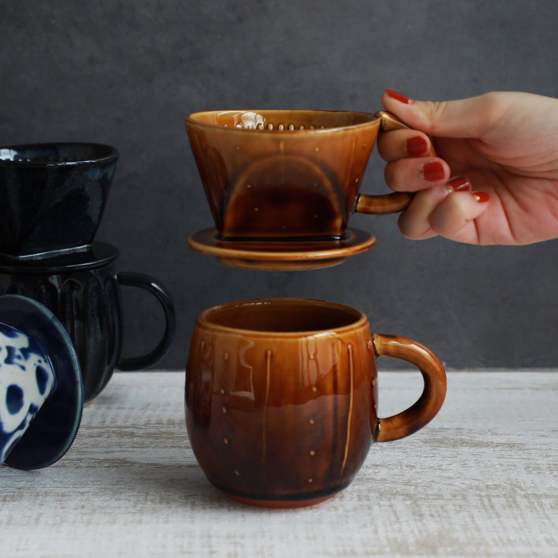 A hand holding the Asayu Japan Ceramic Coffee Dripper in Caramel over the matching accessory mug.