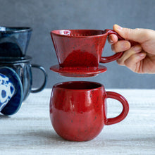 Load image into Gallery viewer, A hand holding the Asayu Japan Ceramic Coffee Dripper in chrome red over the matching accesory mug in chrome red.
