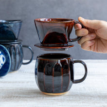 Charger l&#39;image dans la galerie, A hand holding the Asayu Japan Ceramic Coffee Dripper in chocolate brown over the matching accesory mug.

