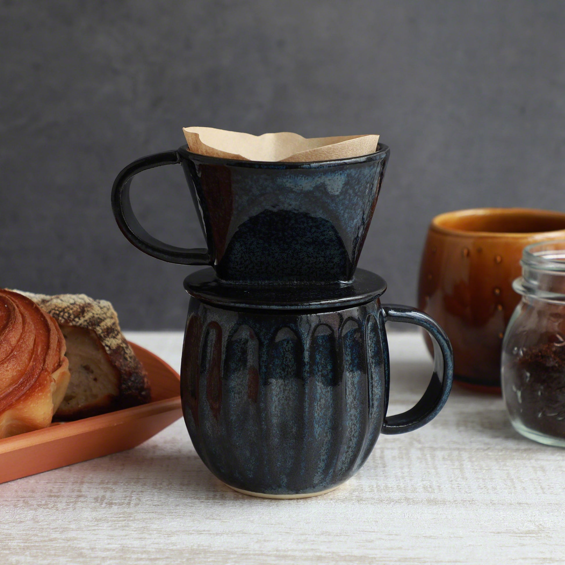 The Asayu Japan Coffee Dripper in dark navy blue put over the accessory mug and with a paper filter on it.