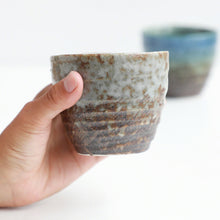 Lade das Bild in den Galerie-Viewer, A hand holding one of the Asayu Japan Handpainted Glazed Ceramic Tea Cups Set of 2 in White glaze
