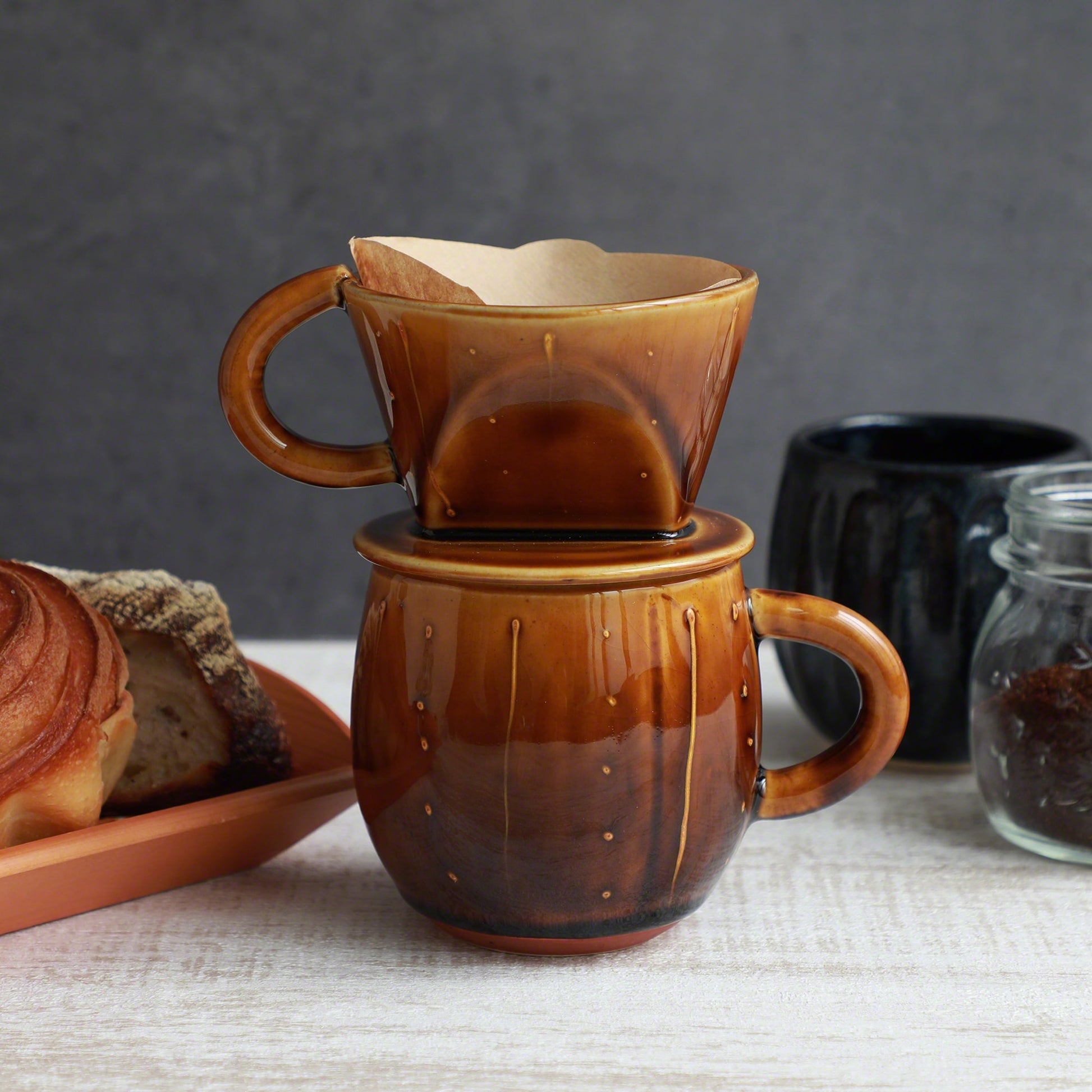 The Asayu Japan Coffee Dripper in caramel put over the accessory mug and with a paper filter on it.