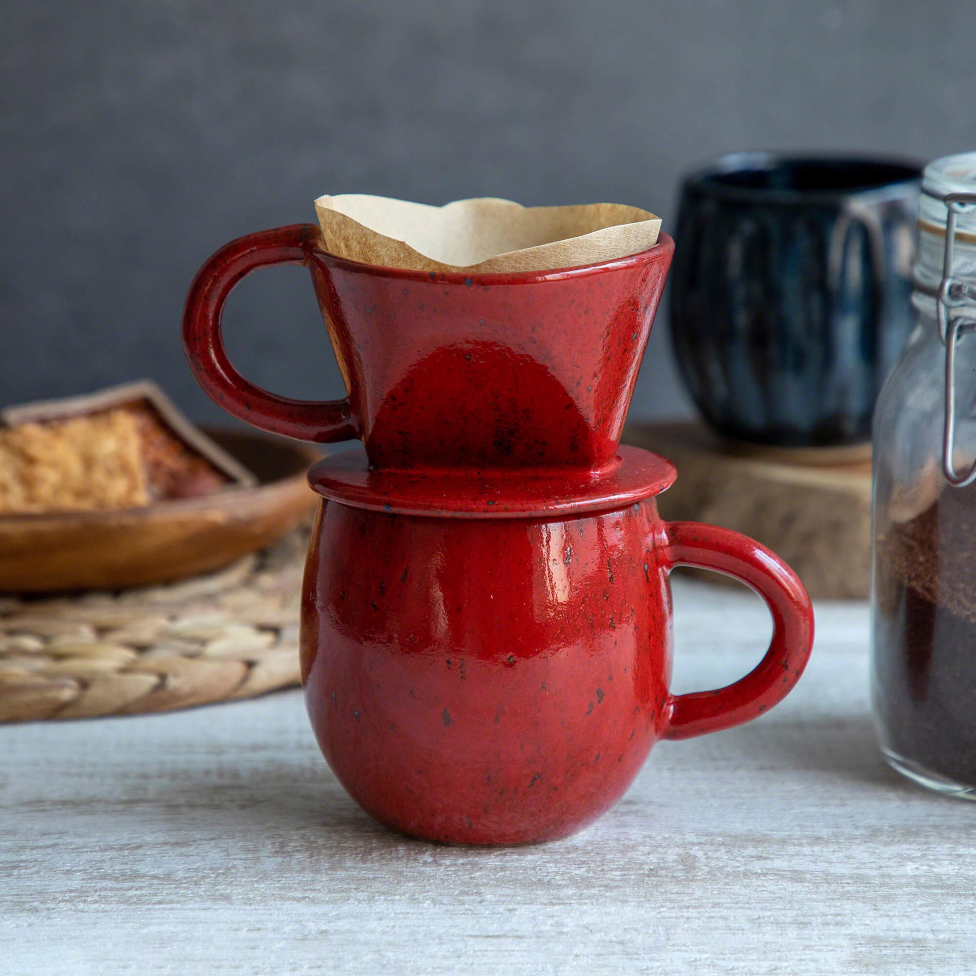 The Asayu Japan Coffee Dripper in chrome red put over the accesory mug in chrome red and with a paper filter on it.