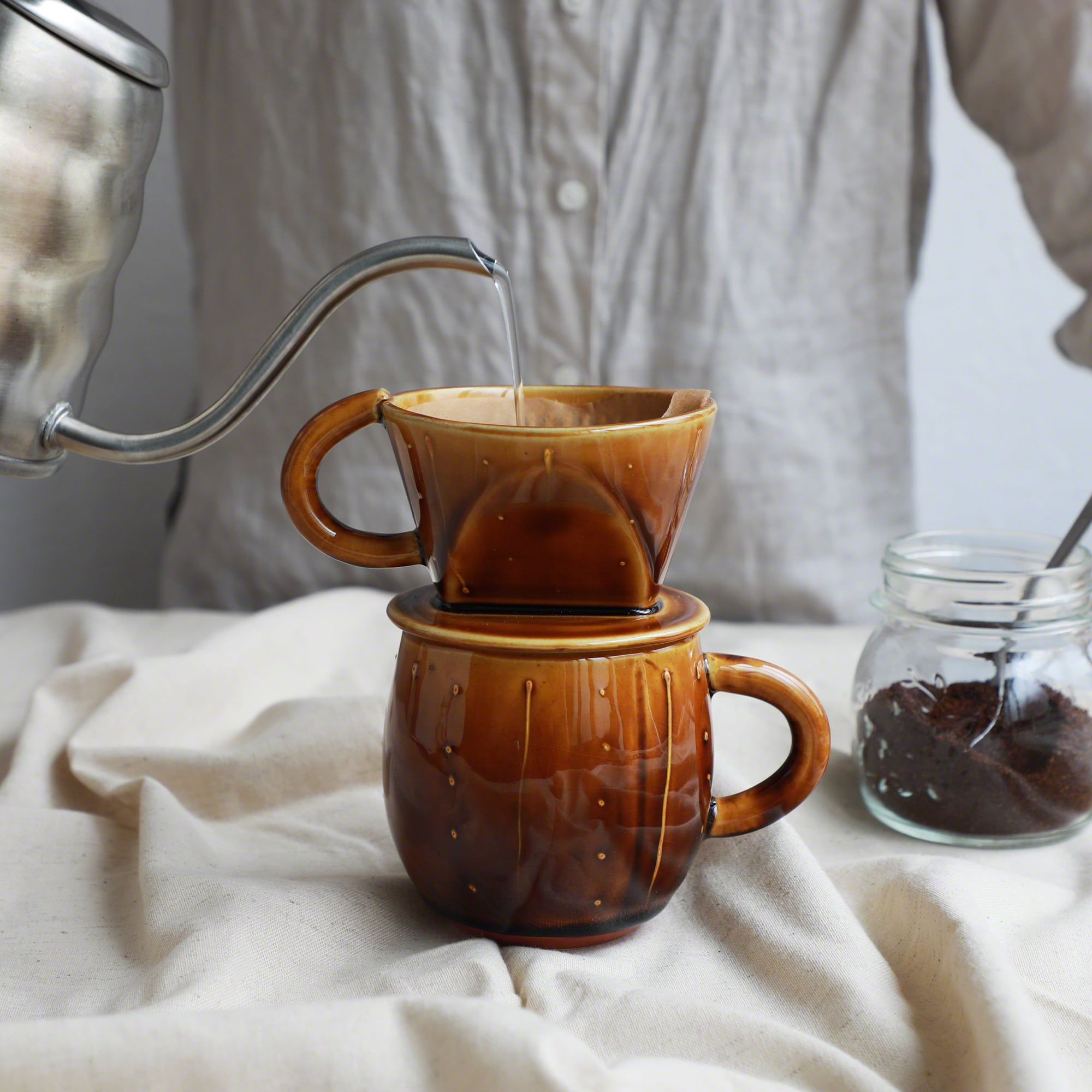 Pouring water over the paper filter on the mounted Asayu Japan Ceramic Coffee Dripper in Caramel to make coffee