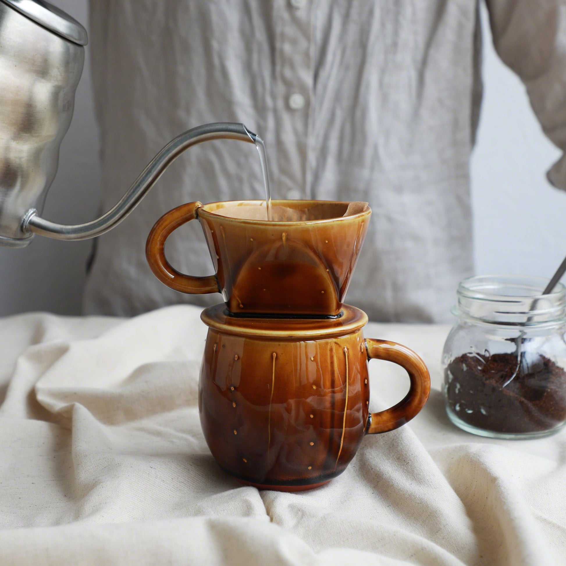 Pouring water over the paper filter on the mounted Asayu Japan Ceramic Coffee Dripper and Accessory Mug in Caramel to make coffee