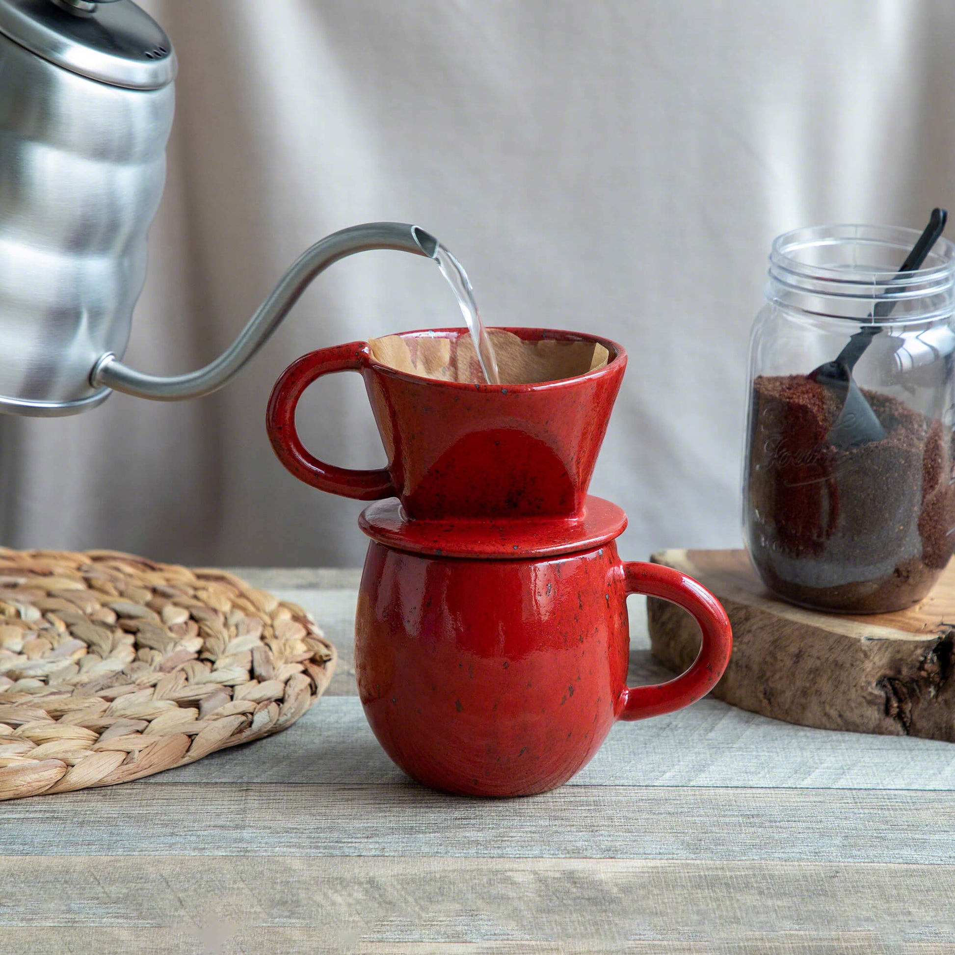 Pouring water over the paper filter on the mounted Asayu Japan Ceramic Coffee Dripper and Accessory Mug in chrome red to make coffee