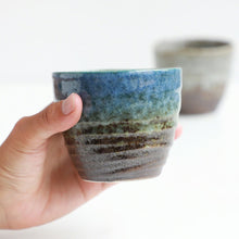 Cargar imagen en el visor de la galería, A hand holding one of the Asayu Japan Handpainted Glazed Ceramic Tea Cups Set of 2 in blue glaze
