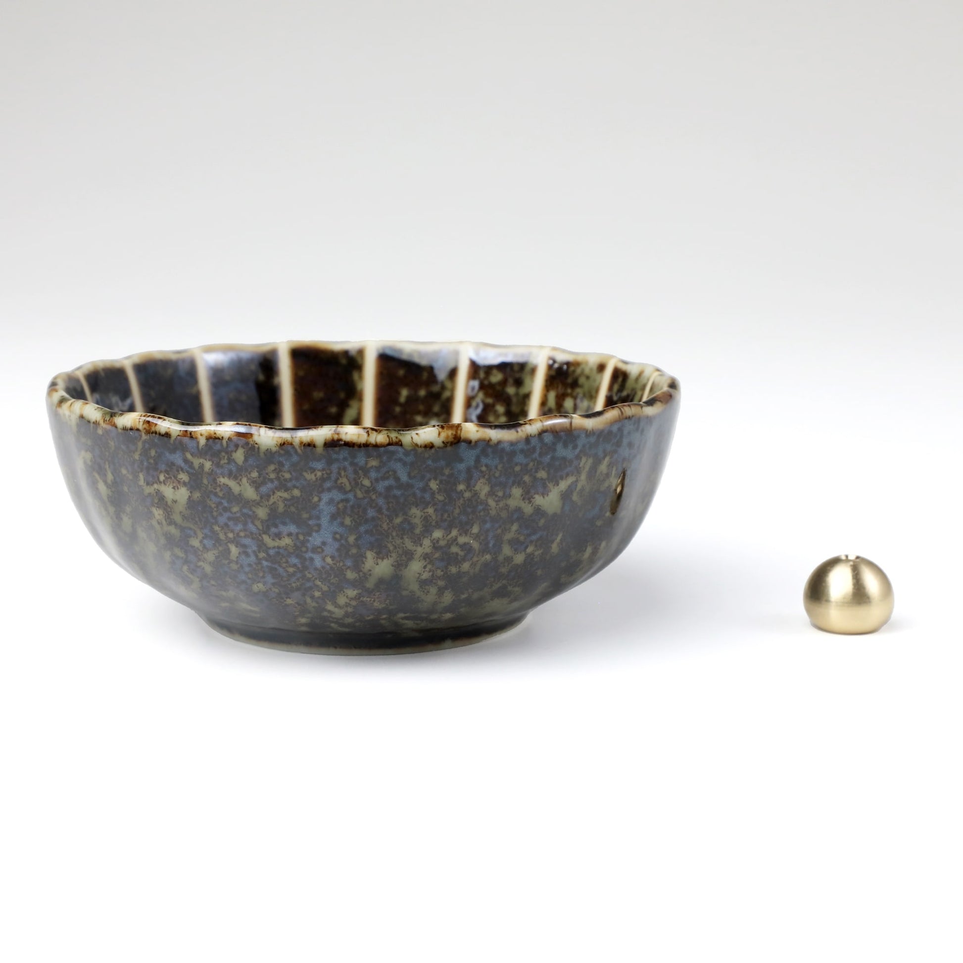 Asayu Japan dark green lotus flower ceramic incense plate with included brass incense burner stand next to it from the side.