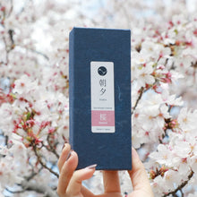 Load image into Gallery viewer, Hand Holding a box of Asayu Japan Sakura Cherry Blossom Low Smoke Incense Sticks in front of a sakura tree
