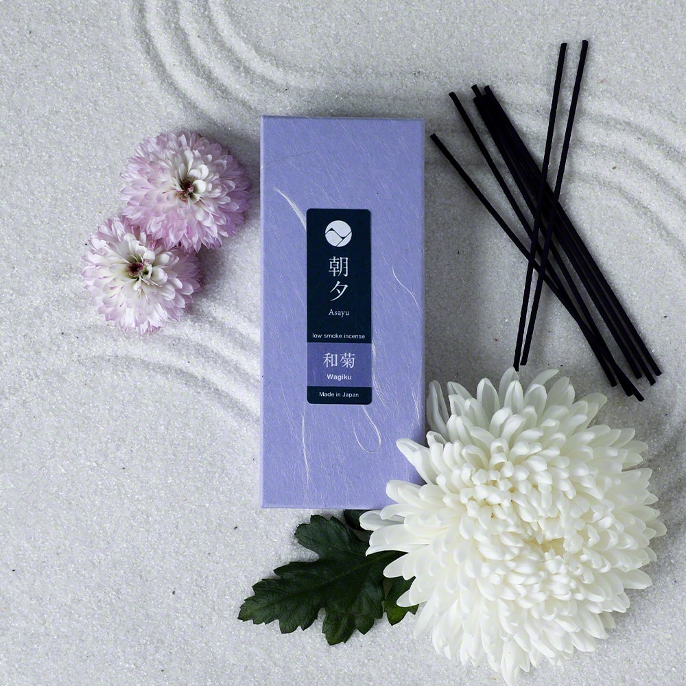 Box of Asayu Japan Wagiku Low Smoke Incense Sticks next to Chrysanthemum flowers in a zen sand tray