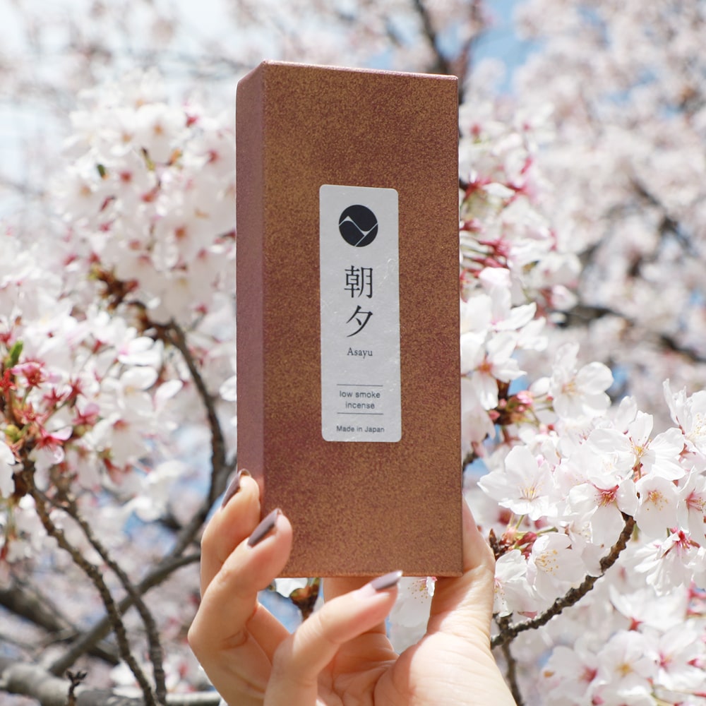 hand holding the sakura incense set in front os cherry blossom flowers